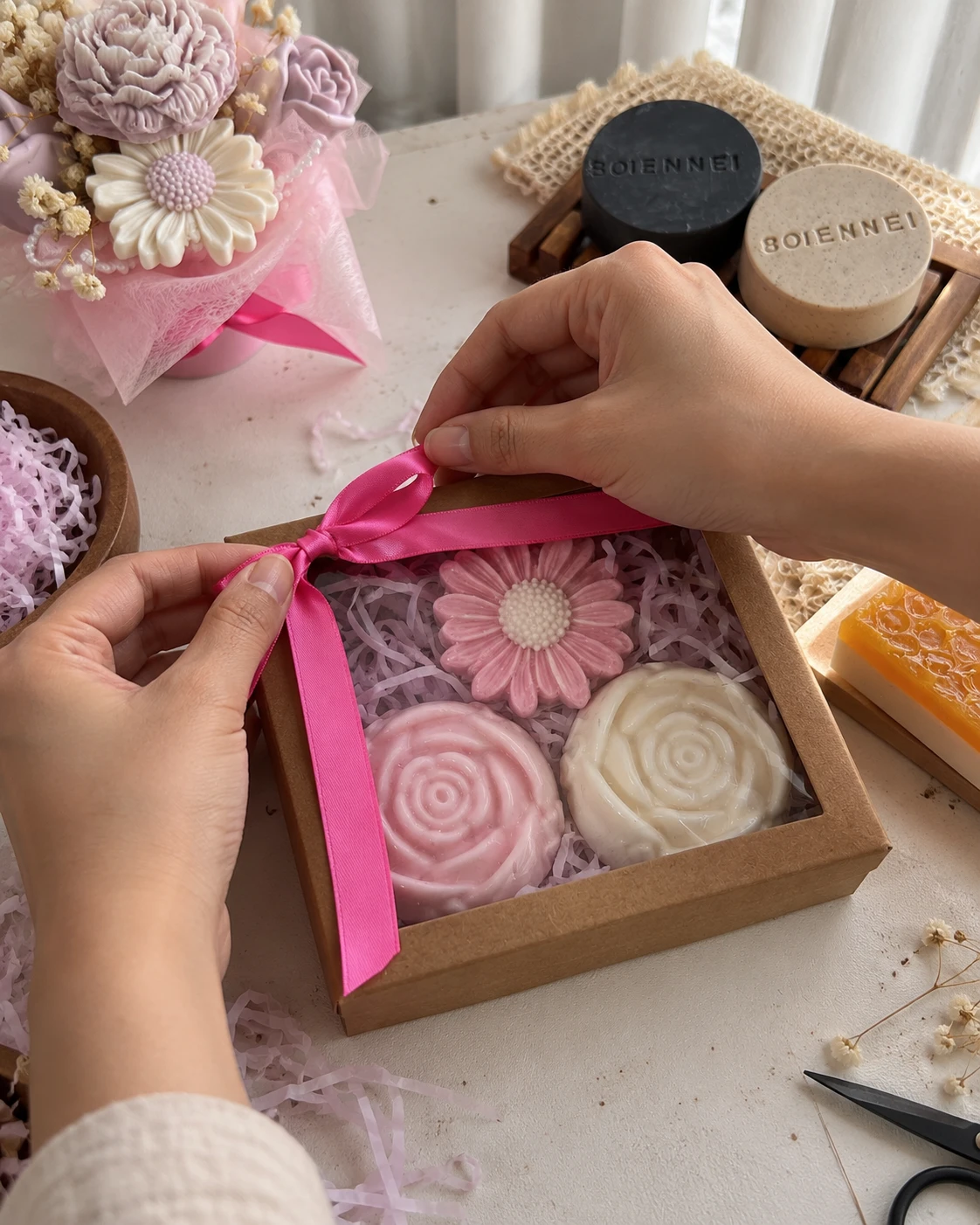 Manos atando un lazo rosado en una caja de jabones artesanales en forma de flor
